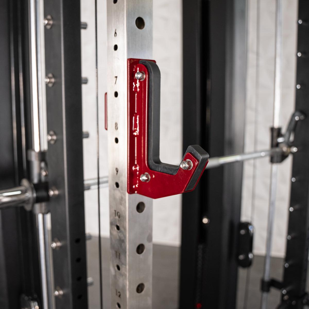 Close-up of a red J-hook with black padding attached to a silver power rack upright.