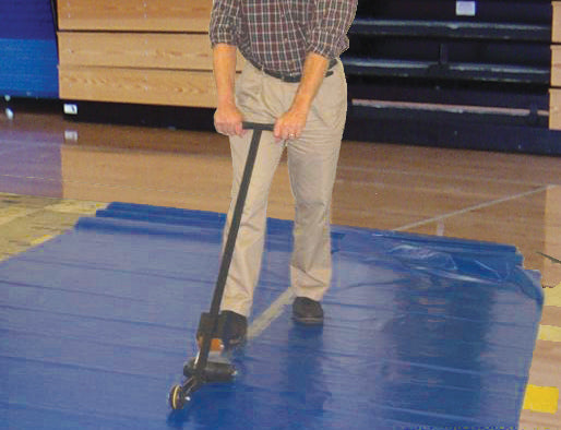 Man rolling a tape dispenser along a seam of a blue vinyl gym floor cover on a wood court
