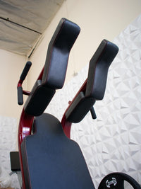 Thumbnail for Close-up of the black padded shoulder rests and back pad of a red plate-loaded squat machine.