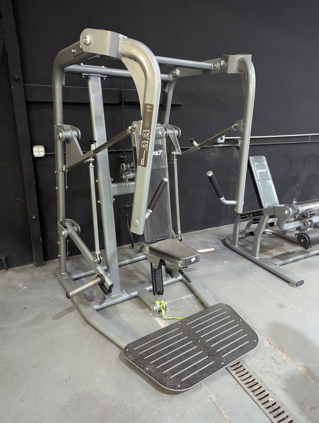 Silver and black chest press machine with a padded seat and foot platform in a gym.