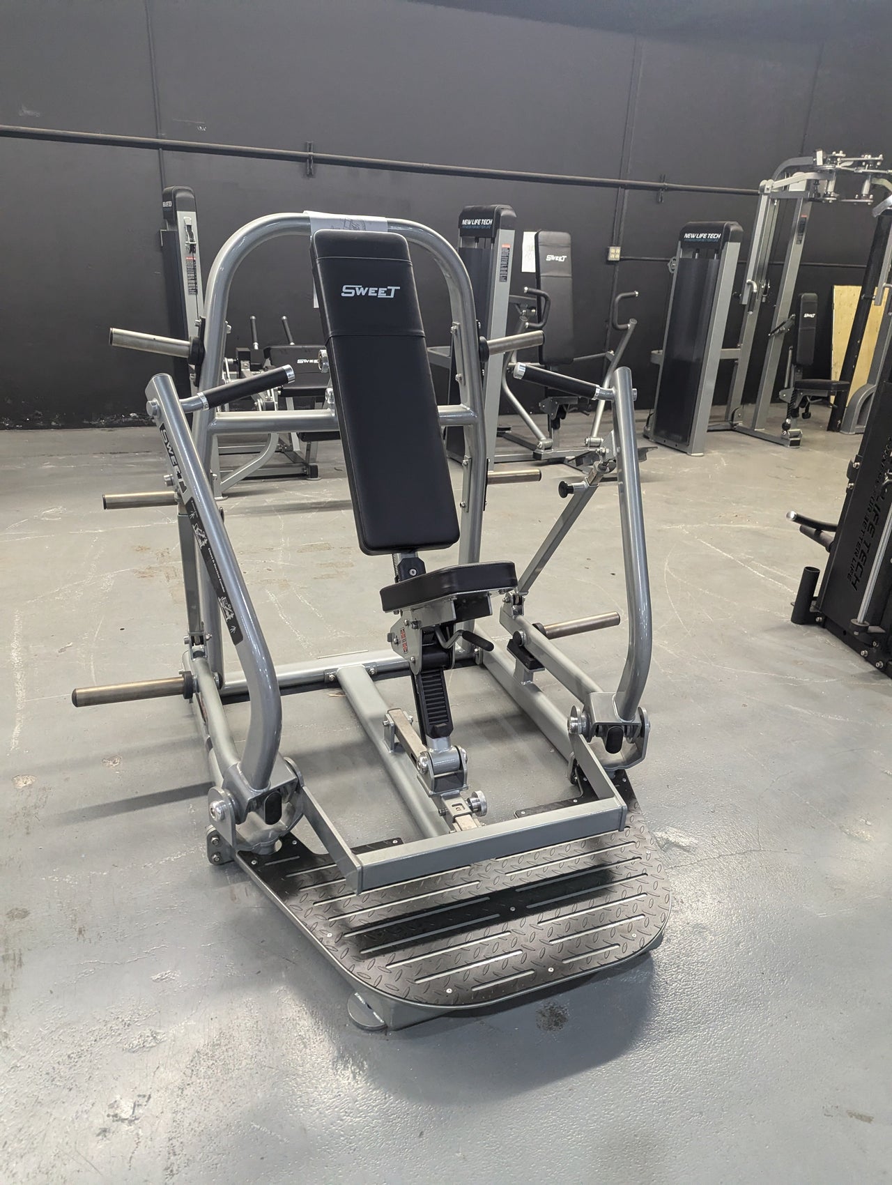 Gray and black Sweet Chest & Decline Combo gym machine with other equipment in the background.