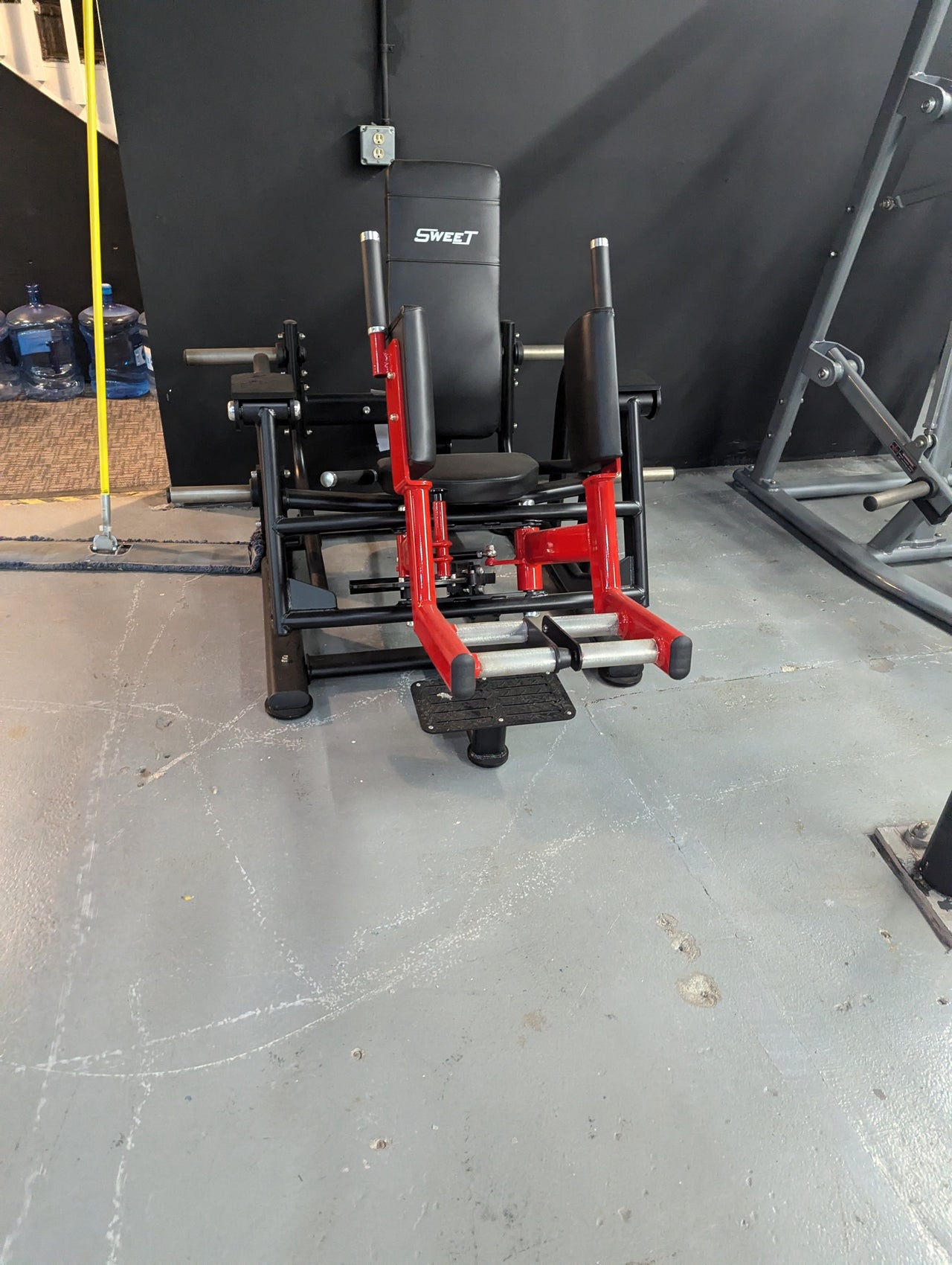 Black and red glute/outer thigh exercise machine with a "SWEET" logo on the backrest.