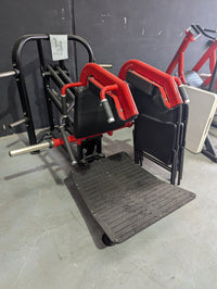 Thumbnail for Black and red hack squat machine with a textured footplate on a gray floor.