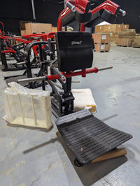 Thumbnail for Red and black hack squat machine with a black footplate on a concrete floor.