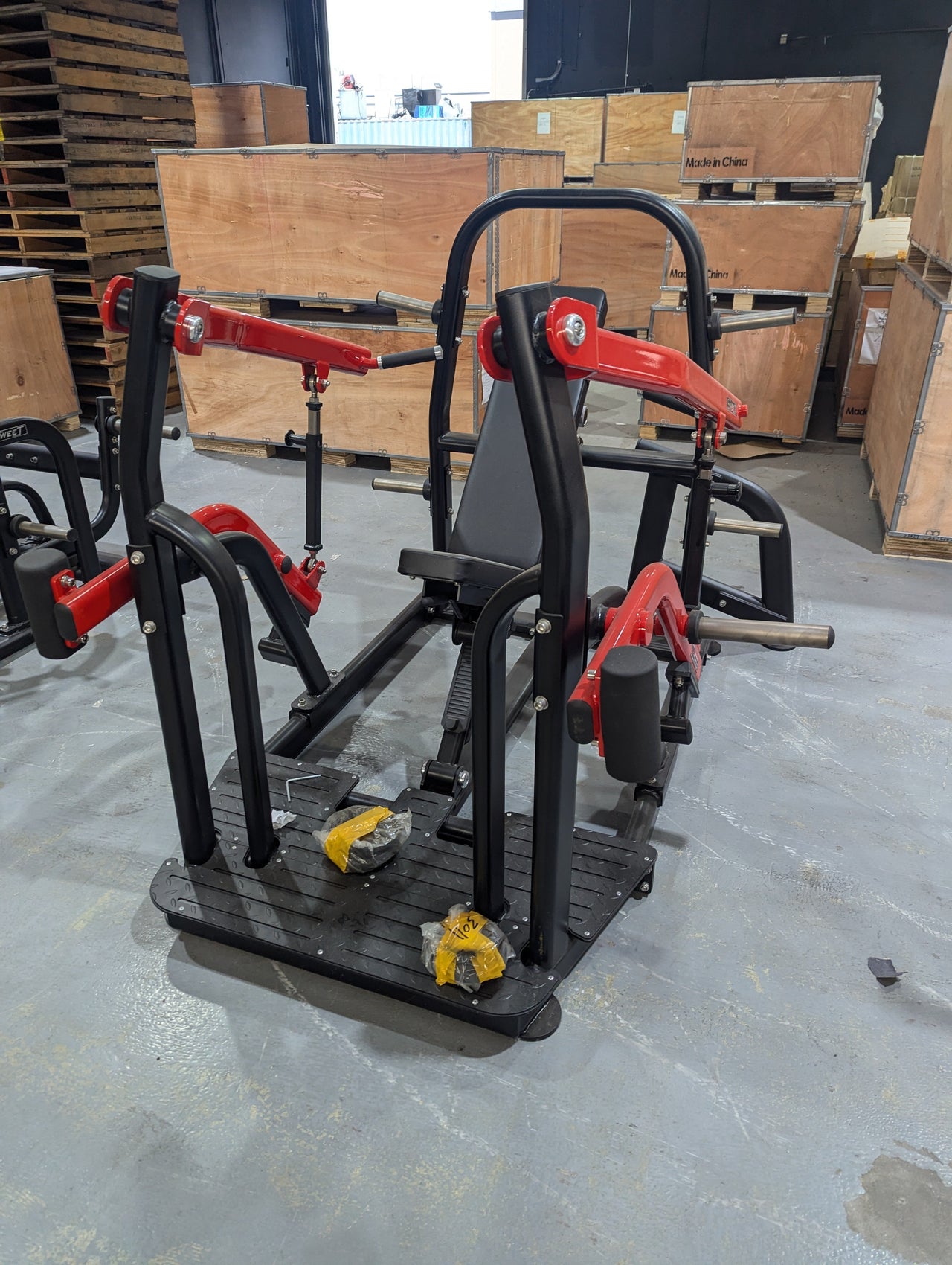 Black and red incline press machine with a padded seat and footrests, in a warehouse setting.