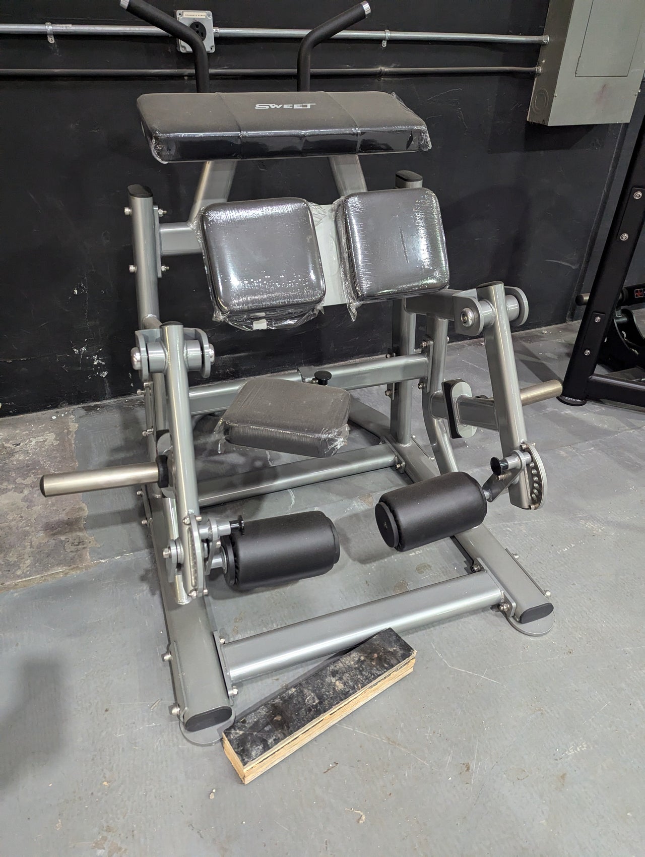 Silver kneeling leg curl machine with black pads and rollers in a gym setting.