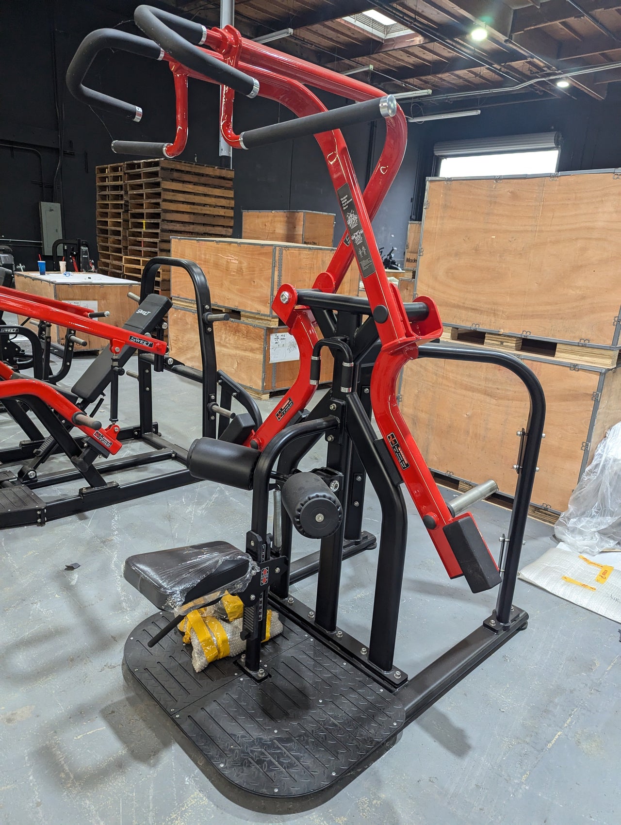 Red and black rotary lat pull-down machine with padded seat and handles in a warehouse setting.