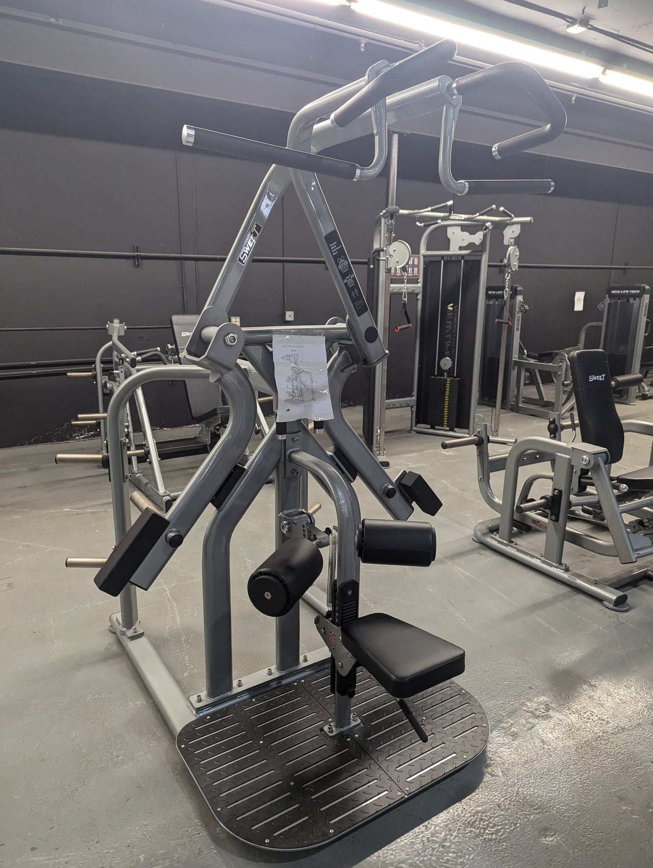 Gray rotary lat pull-down machine with black padded seat and handles in a gym setting.