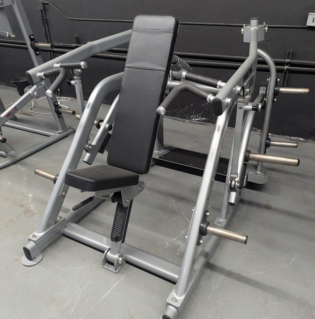 Silver plate-loaded shoulder press machine with black padded seat and backrest in a gym.