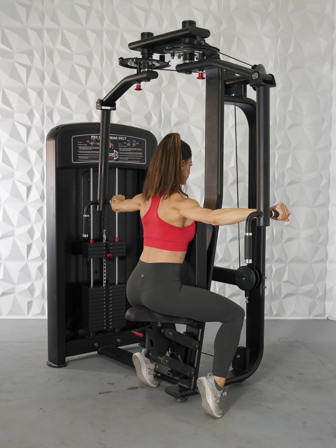 Woman using a black pec deck/rear delt machine with pin selectorized weights.