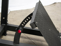 Thumbnail for Close-up of a black adjustable footplate with a textured surface and a red adjustment knob on a squat machine.