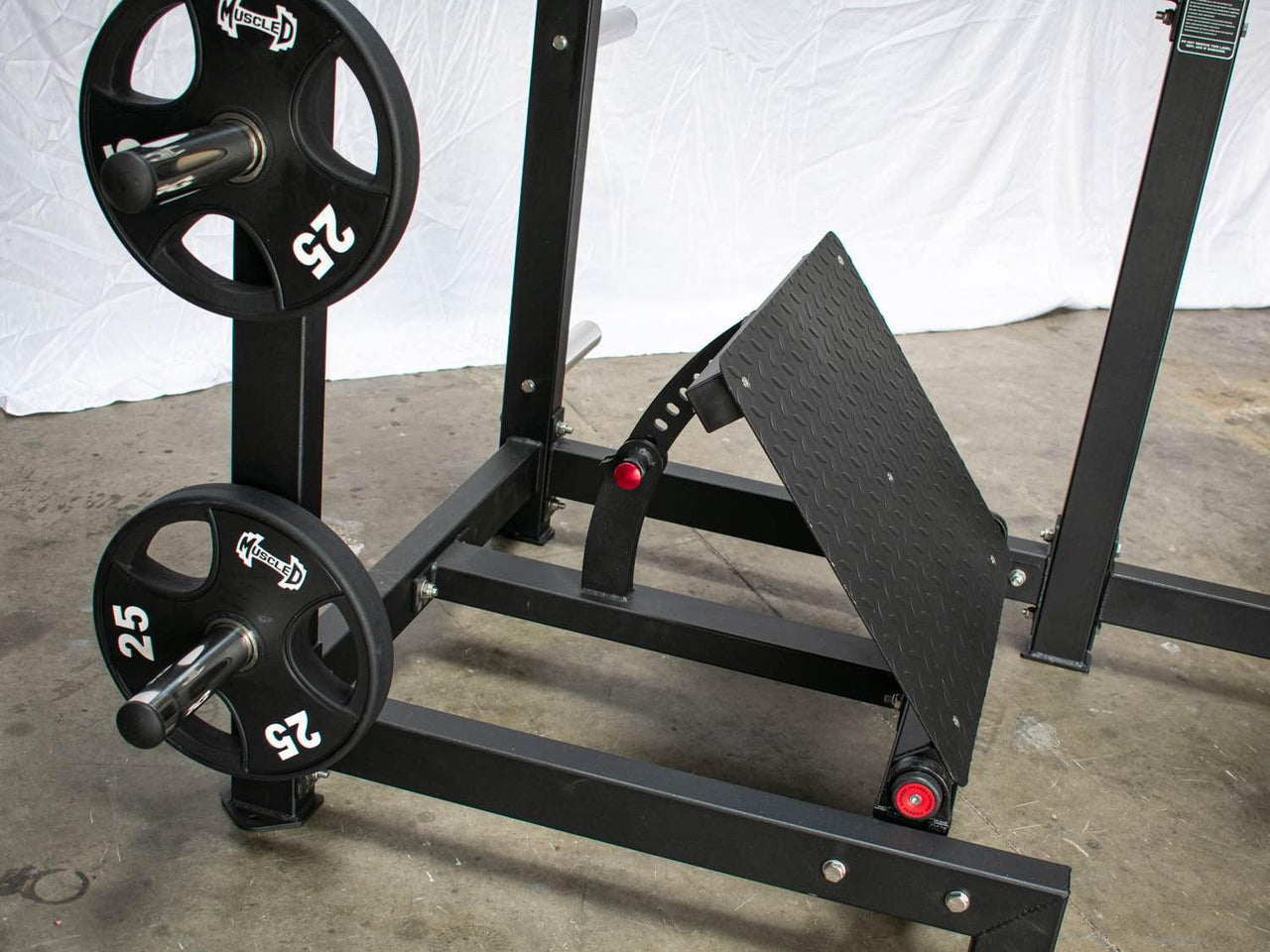 Black plate-loaded squat machine with 25lb weights on storage pegs and an adjustable footplate.