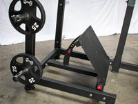 Thumbnail for Black plate-loaded squat machine with 25lb weights on storage pegs and an adjustable footplate.