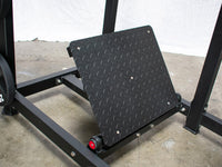 Thumbnail for Close-up of the black diamond-plate foot platform of a squat machine, with a 25lb weight plate visible.
