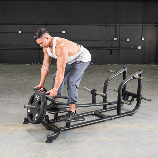 Man in a white tank top using a black T-bar row machine with a 45lb weight plate.