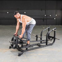 Thumbnail for Man in a white tank top using a black T-bar row machine with a 45lb weight plate.