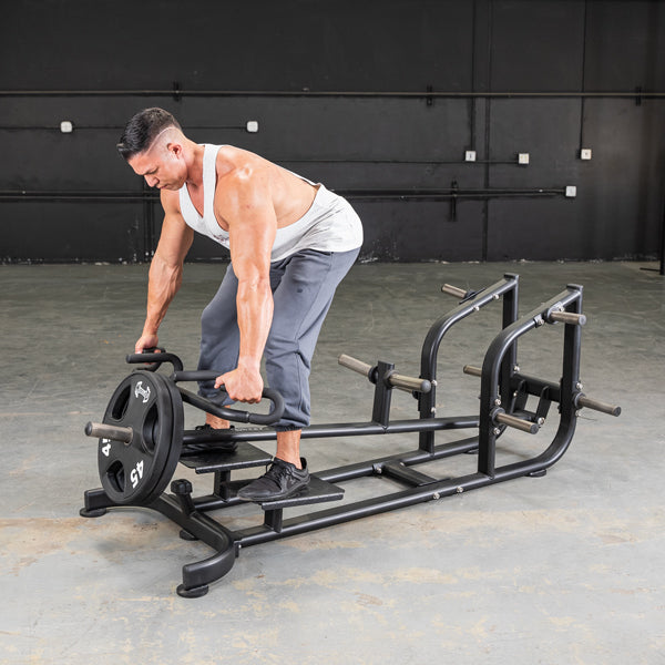 Man using a black T-bar row machine with weight plates in a gym.