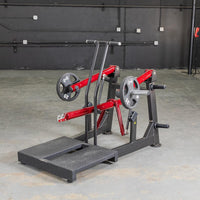 Thumbnail for Black and red belt squat machine with weight plates on a concrete floor.