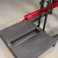 Thumbnail for Close-up of the black diamond plate foot platform and red lever arm with hooks on a belt squat machine.