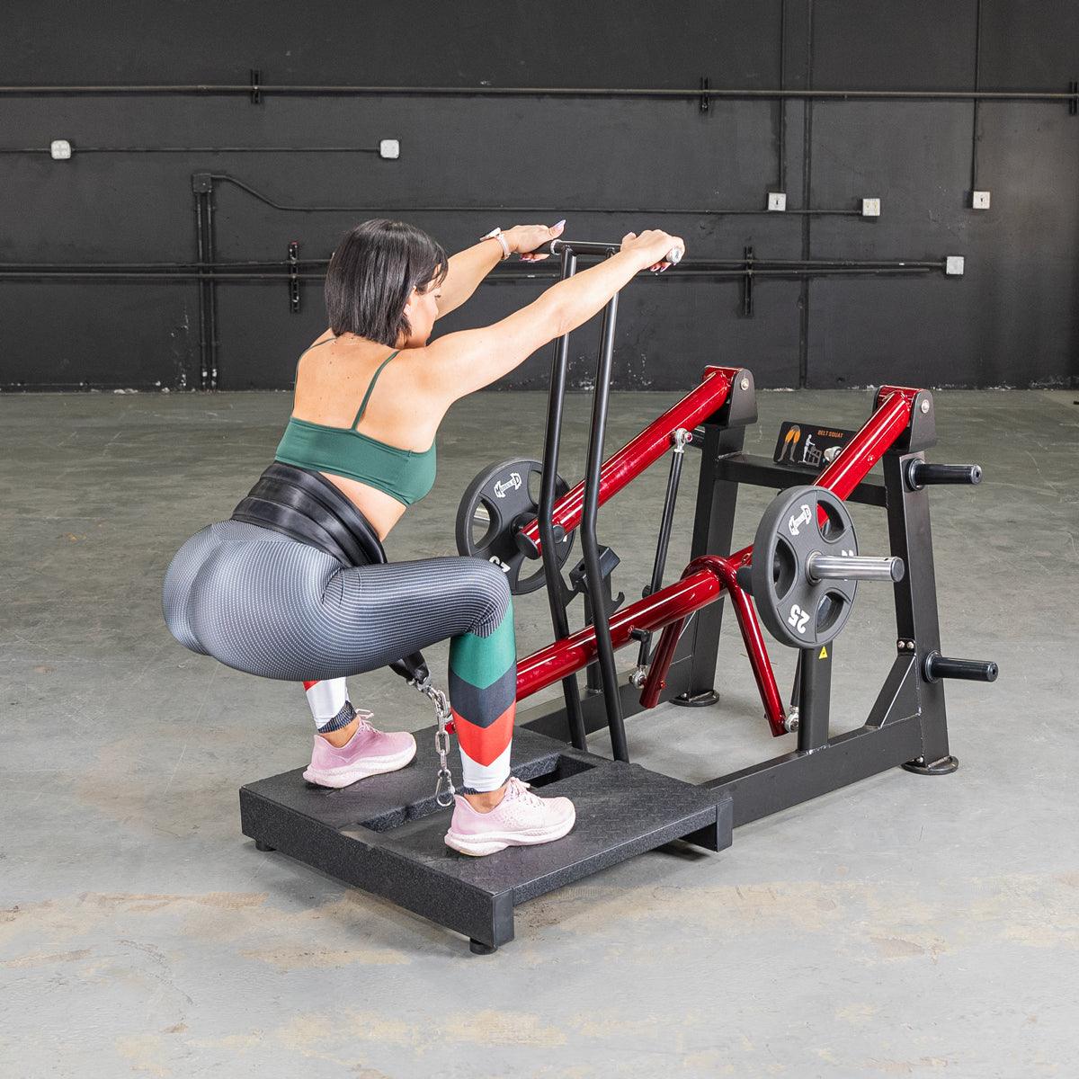 Woman performing a belt squat on a red and black Power Leverage V2 machine with weight plates.