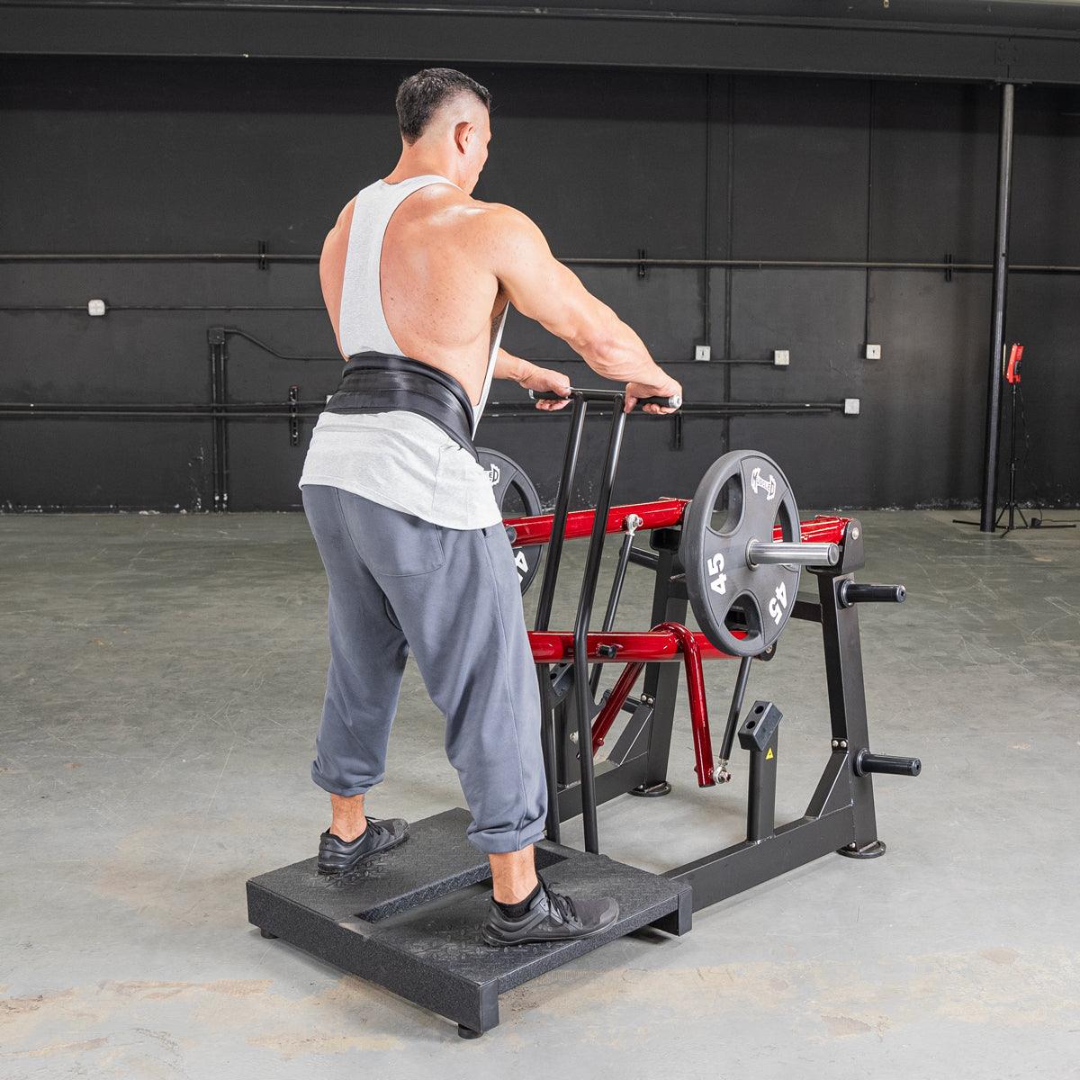 Man performing belt squats on a black and red Power Leverage V2 machine with weight plates.