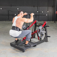 Thumbnail for Man in a gym using a red and black belt squat machine with weight plates.