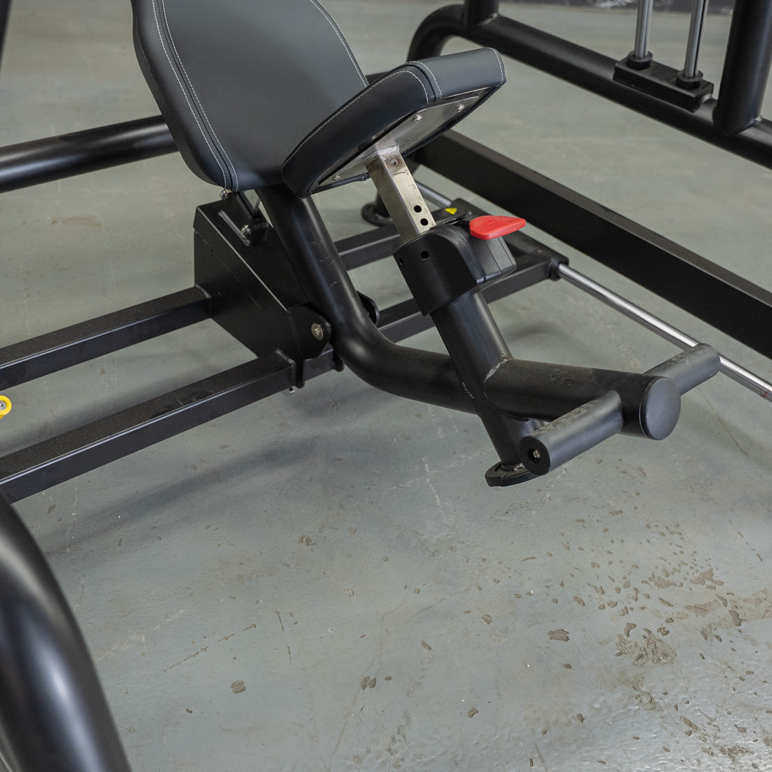 Close-up of a black gym bench's seat and adjustable leg rest with a red lever.