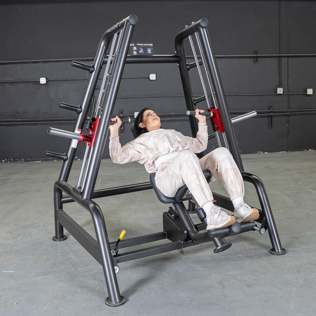 Woman performing an incline press on a black Power Leverage V2 Convergent Bench in a gym.