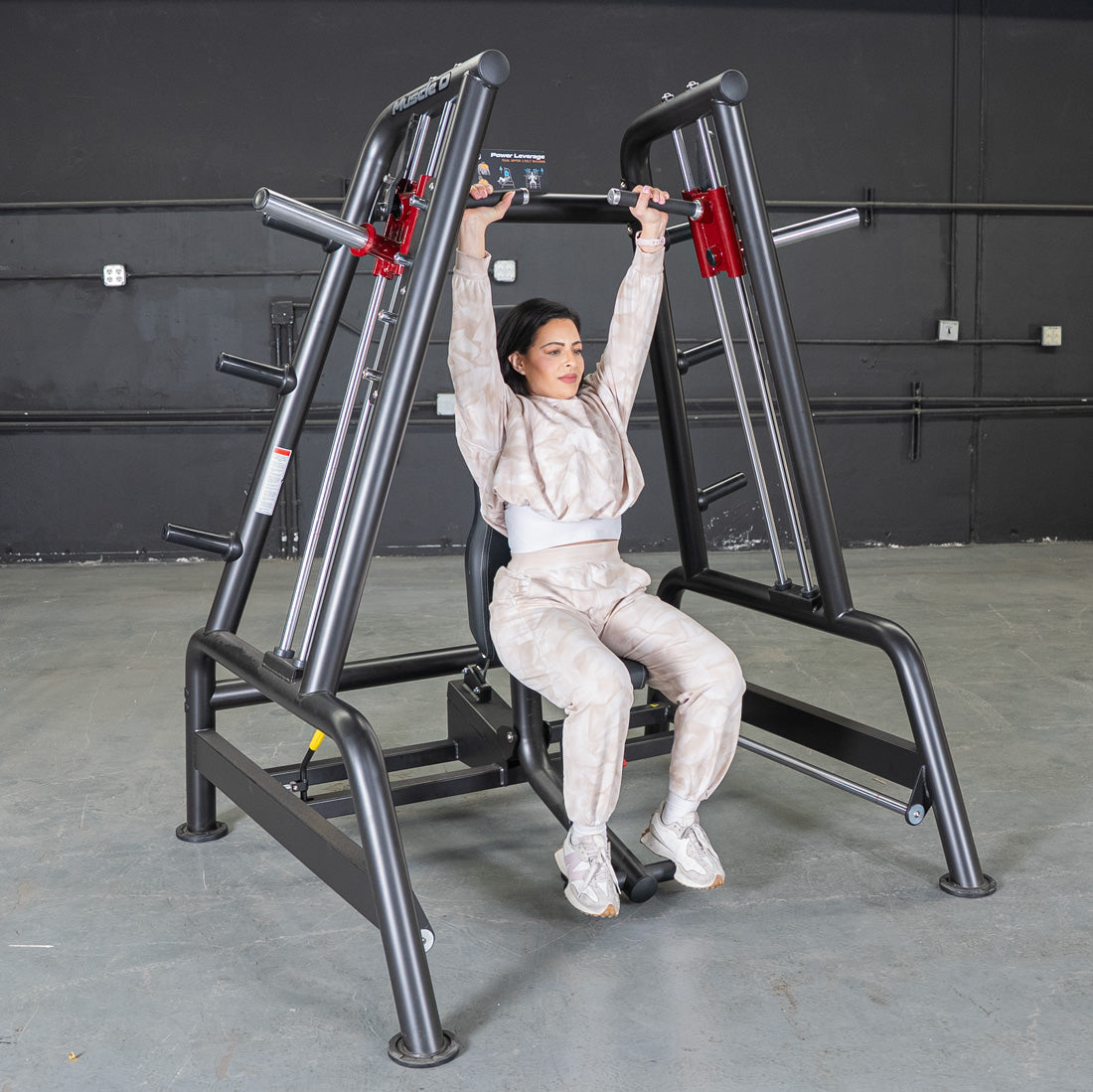Woman using a Power Leverage V2 Convergent Bench for shoulder press, arms extended overhead.