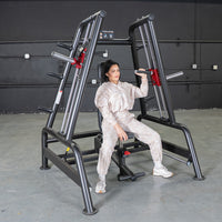 Thumbnail for Woman seated on a black leverage bench machine, holding handles for a shoulder press exercise.