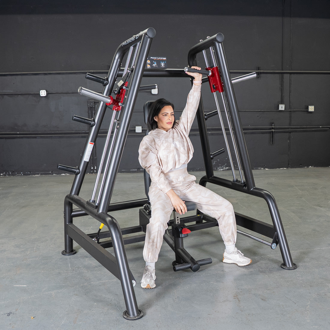 Woman using a black and red Power Leverage V2 Convergent Bench for a shoulder press in a gym.