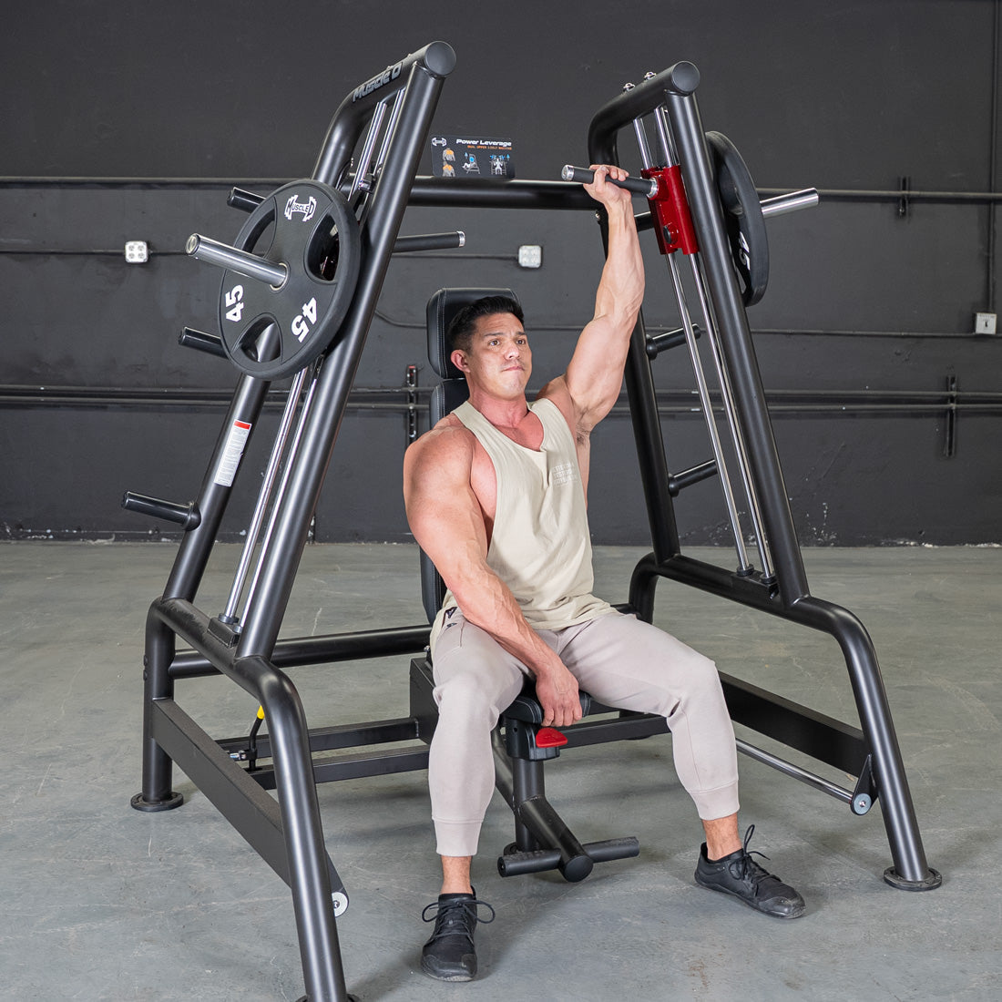 Man performing a shoulder press on a black Power Leverage V2 Convergent Bench with 45lb plates.
