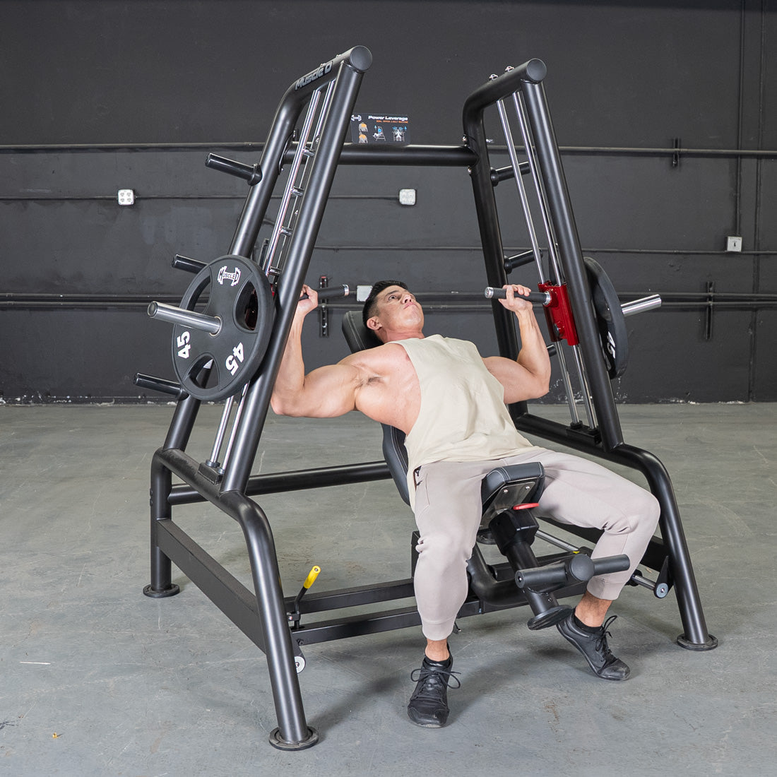 Man using a black incline bench press machine with weight plates in a gym.