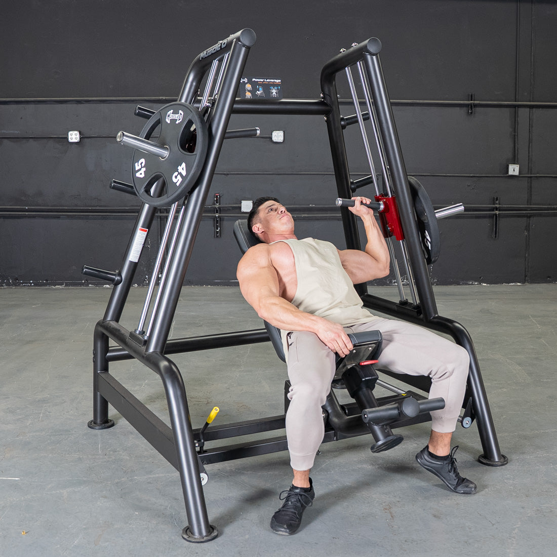 Muscular man performing incline shoulder press on a black leverage bench with weight plates.