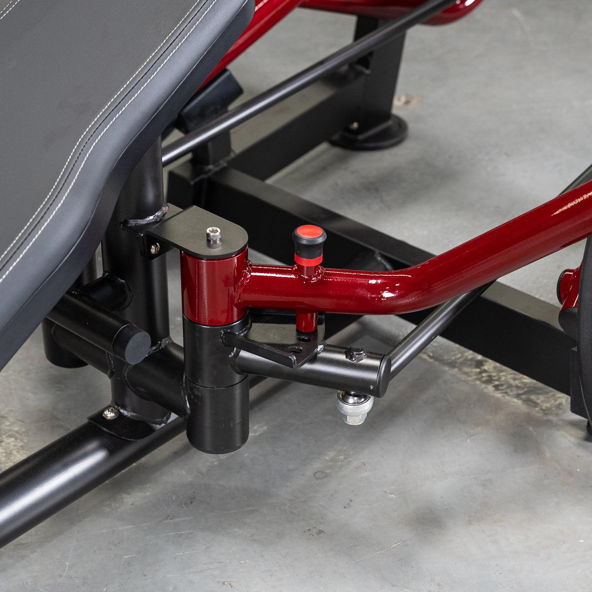 Close-up of the red and black frame of a fitness machine with a black padded bench on the left.