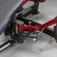Thumbnail for Close-up of the red and black frame of a fitness machine with a black padded bench on the left.