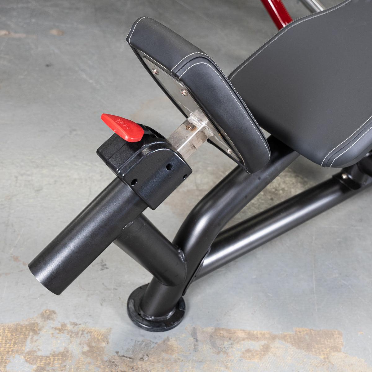 Black fitness machine with padded seat, red adjustment lever, and sturdy metal frame on a concrete floor.