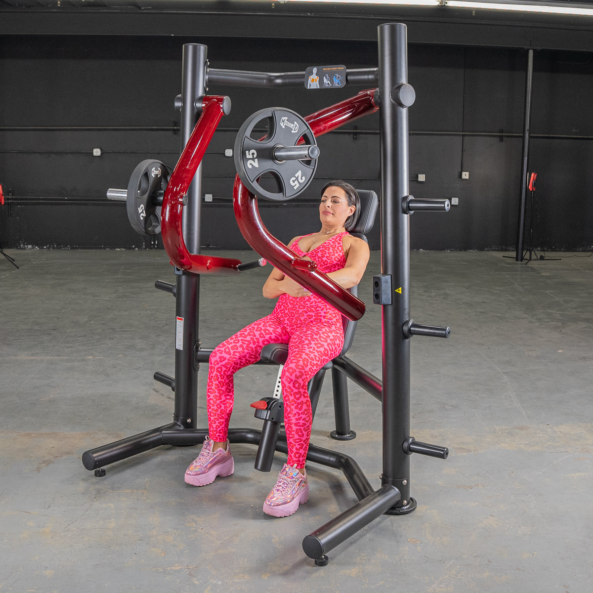 Woman in pink leopard print workout gear seated on a black and red decline chest press machine.