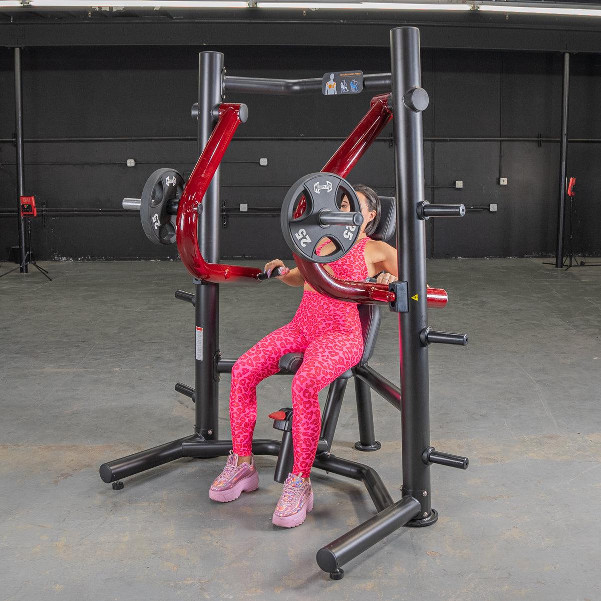 Woman in pink leopard print using a red and black decline chest press machine with weight plates.