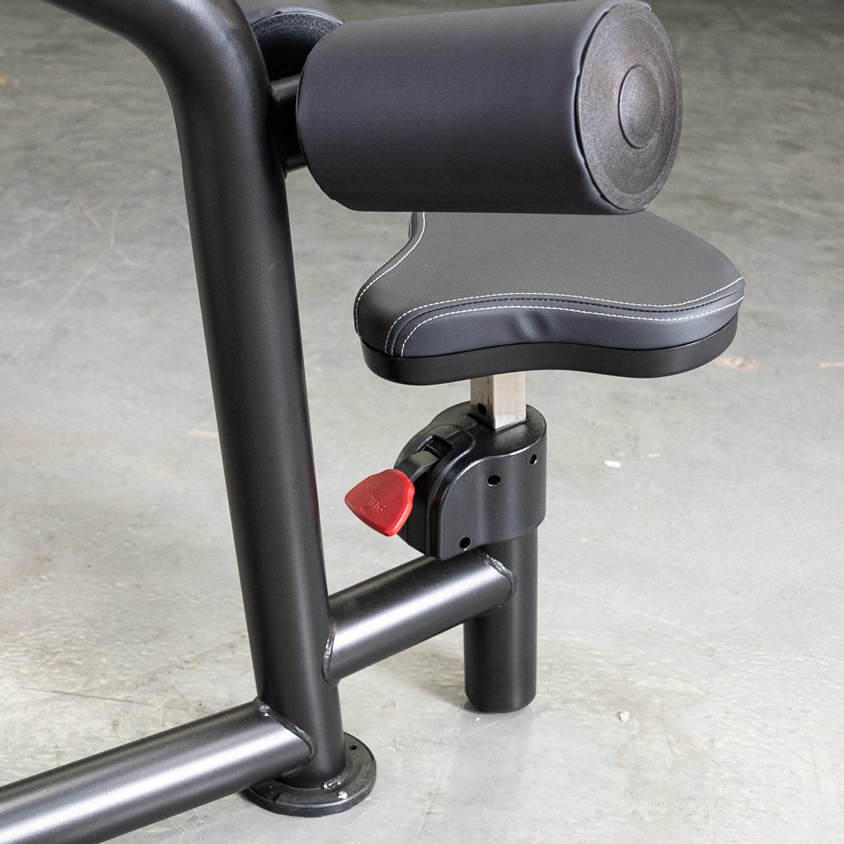 Close-up of a black fitness machine's seat and leg pad with a red adjustment lever.