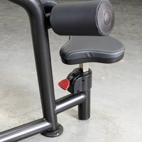 Thumbnail for Close-up of a black fitness machine's seat and leg pad with a red adjustment lever.