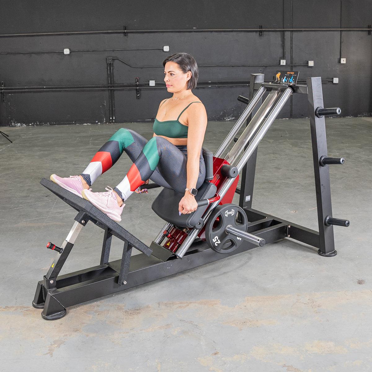 Woman performing hack squats on a black and red fitness machine with a 25lb weight plate.