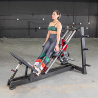 Thumbnail for Woman using a black and red hack squat machine with a 25lb weight plate in a gym.