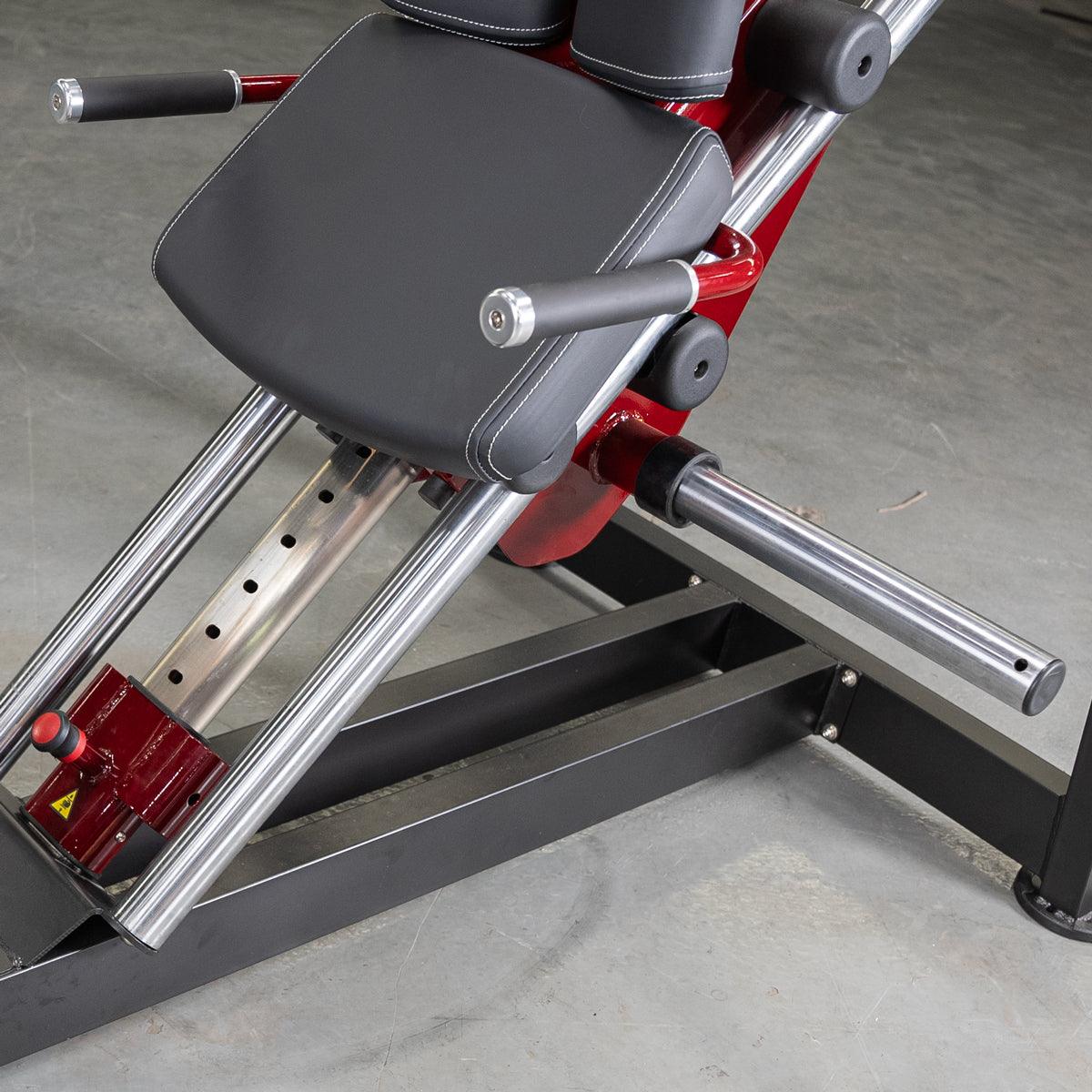 Close-up of a red and black hack squat machine with padded backrest and handles.