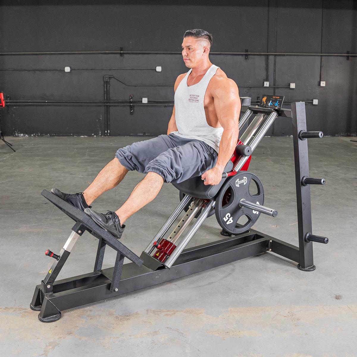 Man in white tank top and gray shorts using a hack squat machine with 45lb weights.