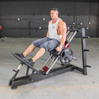 Thumbnail for Man in white tank top and gray shorts using a hack squat machine with 45lb weights.