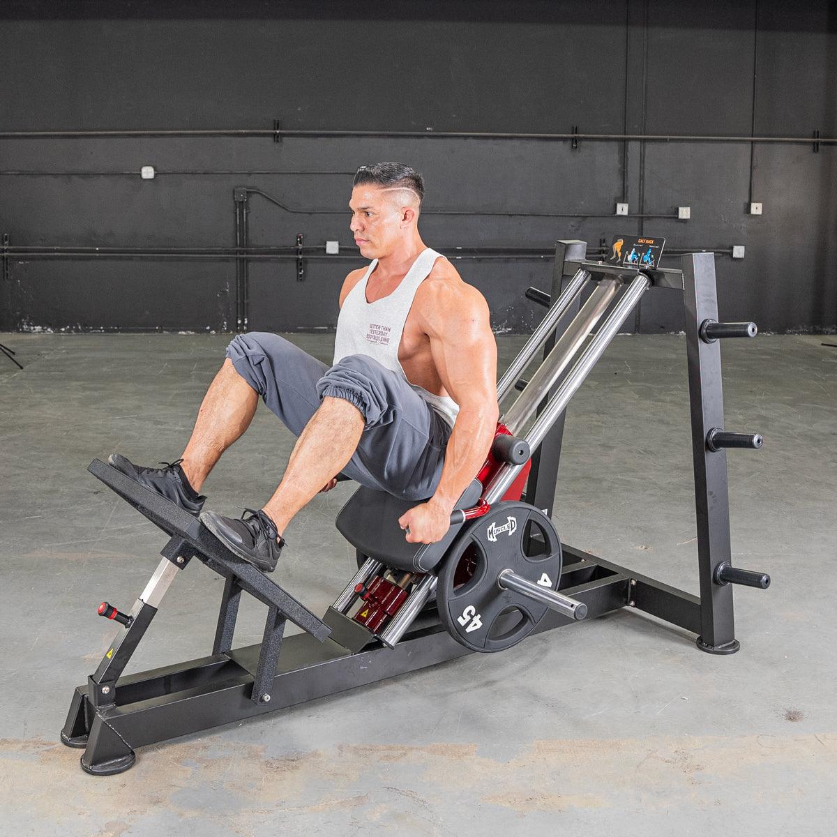 Man in white tank top using a black and red hack squat machine with 45lb weight plates in a gym.
