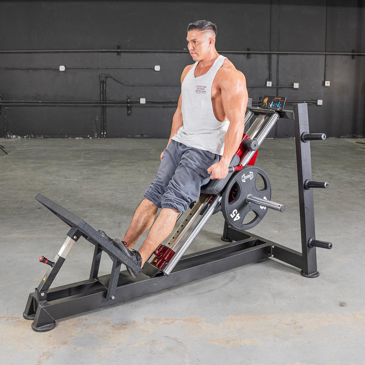 Man performing hack squat on a black and red machine with a 45lb weight plate.