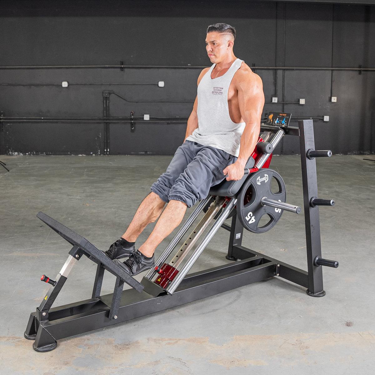 Man using a black and red hack squat machine with a 45lb weight plate in a gym.