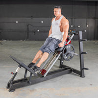 Thumbnail for Man using a black and red hack squat machine with a 45lb weight plate in a gym.